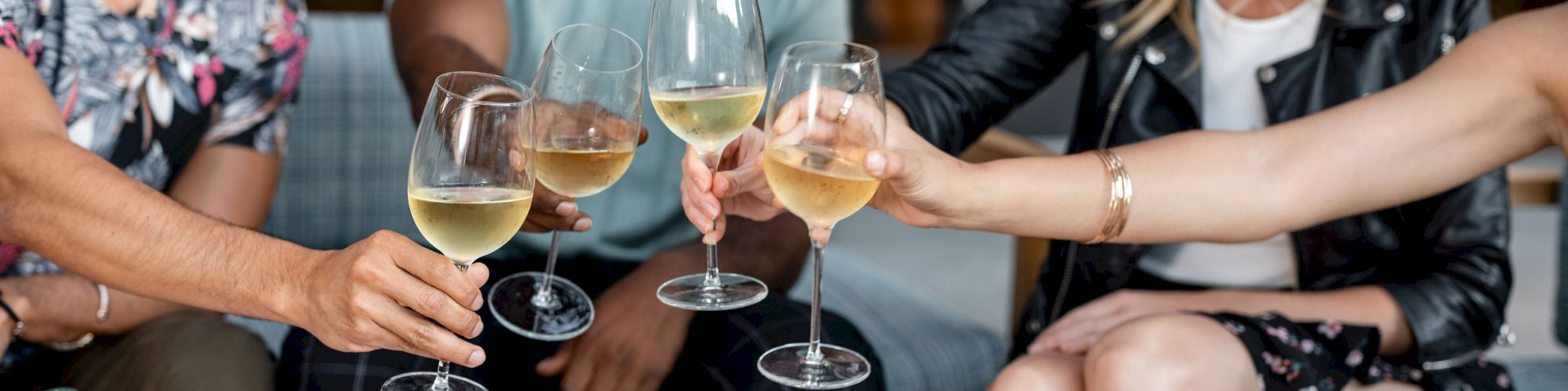 People are toasting with glasses of white wine around a table with food containers.