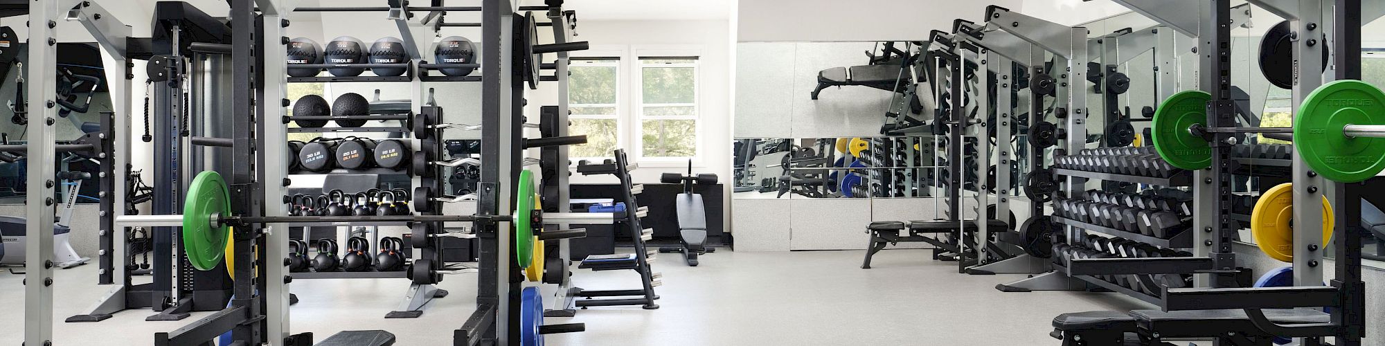 This image shows a well-equipped gym with various weightlifting and exercise machines, free weights, and mirrors on the walls.