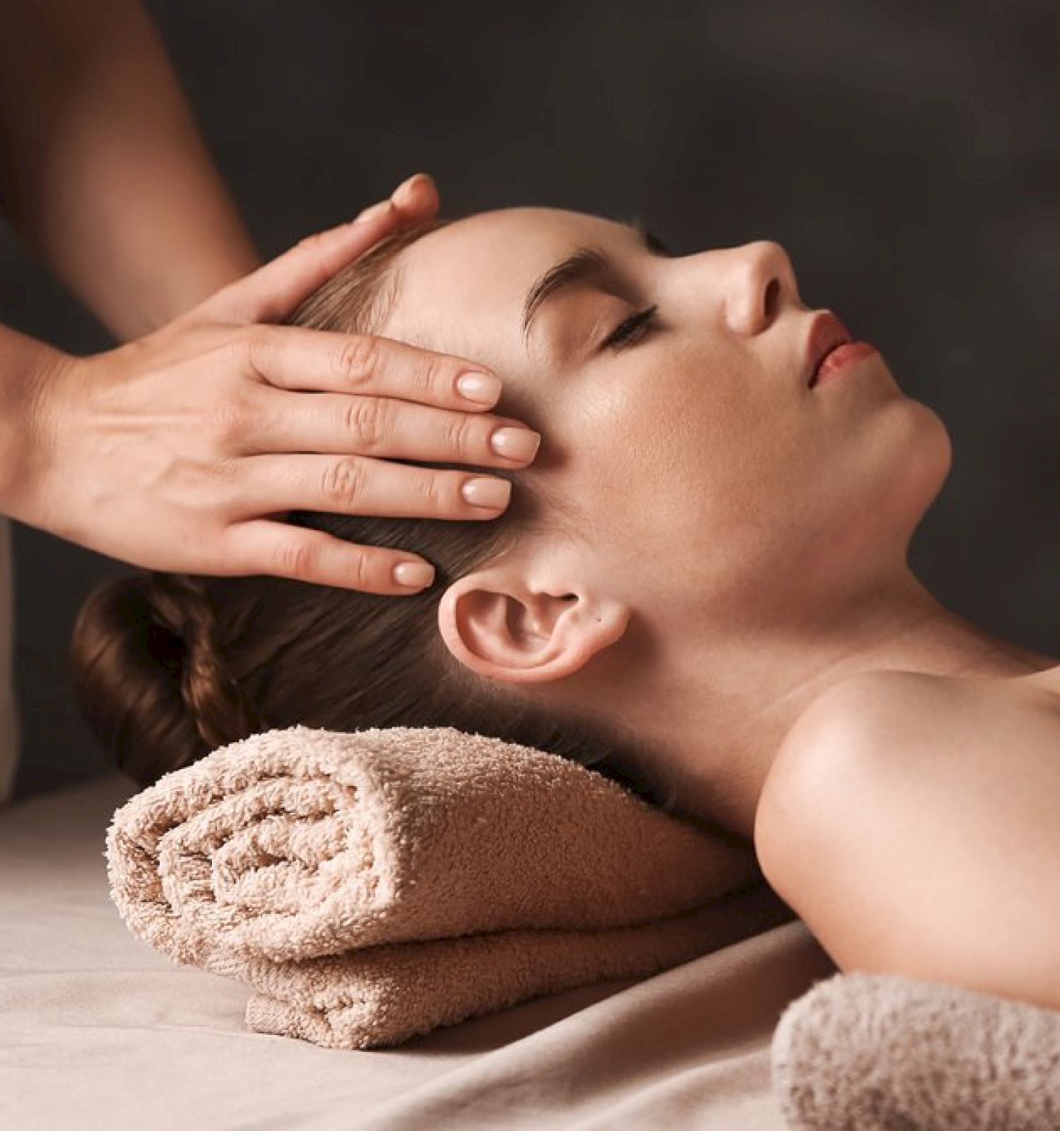 A person is receiving a relaxing head massage while lying on a table with a rolled towel under their head, covered partially by another towel.