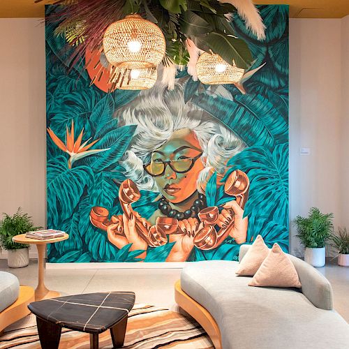 A room with colorful wall art featuring a woman, modern furniture, plants, and hanging light fixtures with greenery above.