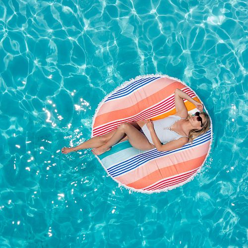 A person in a swimsuit is lounging on a colorful float in a pool, enjoying the sunny day and the refreshing water.