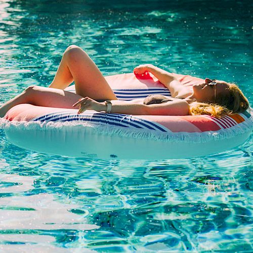 A person is lounging on an inflatable float in a swimming pool, enjoying the sunlight and relaxing. The water is clear and blue.