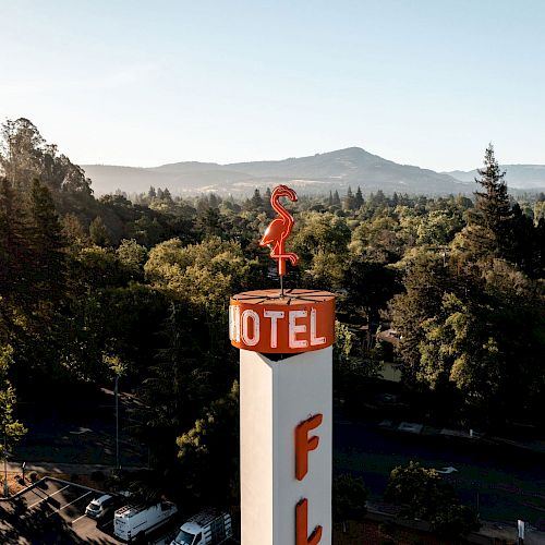 An aerial photo shows a tall sign reading "MOTEL" with a red flamingo on top, surrounded by a lush green landscape with mountains in the distance.