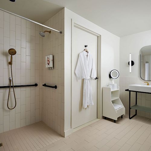 A modern bathroom features a walk-in shower, a hanging white robe, a large mirror, a sink, and minimalist decor, creating a clean and elegant space.