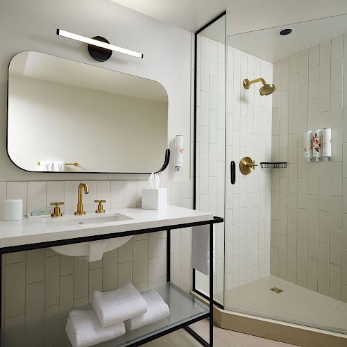 The image shows a modern bathroom with a large mirror, a vanity with a golden faucet, and a glass-enclosed shower with gold fixtures.