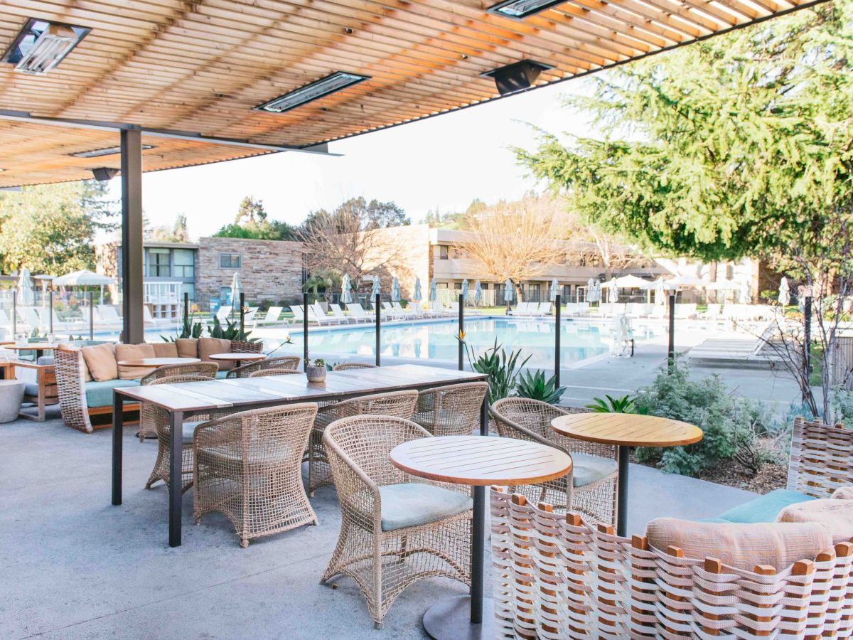 An outdoor seating area with wicker furniture and tables, overlooking a swimming pool and surrounded by trees.