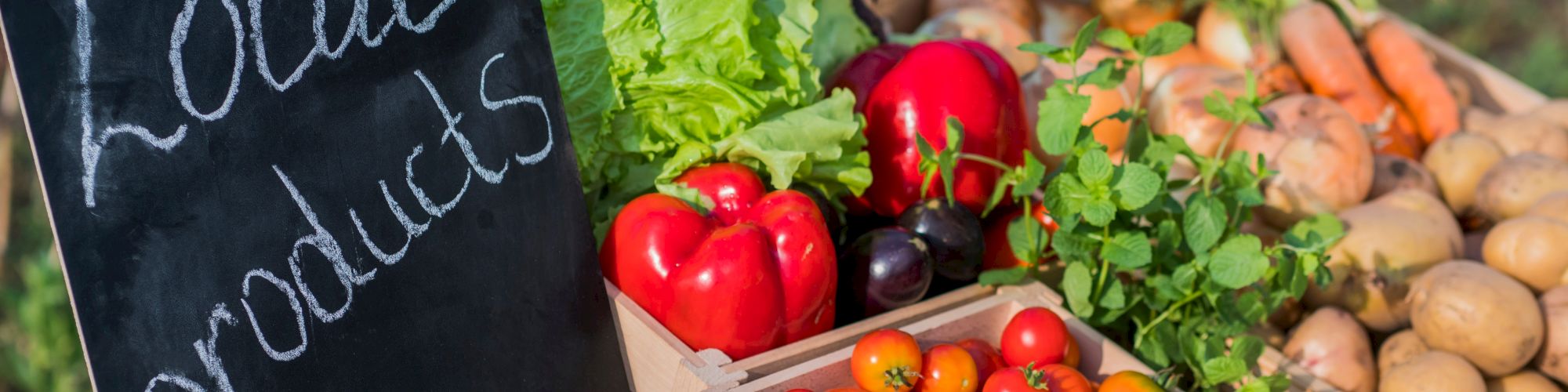 A display of fresh vegetables including tomatoes, peppers, carrots, and lettuce, with a chalkboard sign reading "Local products."