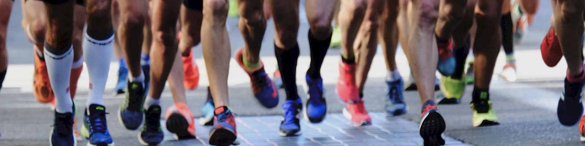 A group of runners in athletic wear are participating in a race, with visible focus on their legs and running shoes as they move forward.