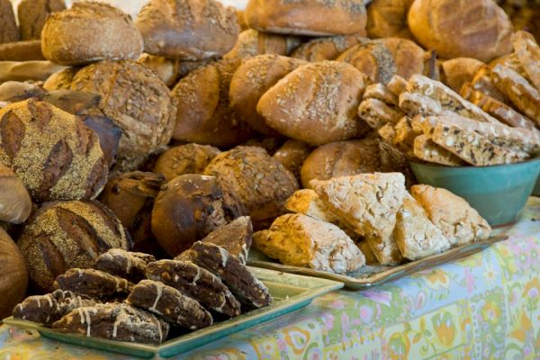 The image shows an assortment of freshly baked bread and pastries arranged on a table, including loaves, scones, and cookies.