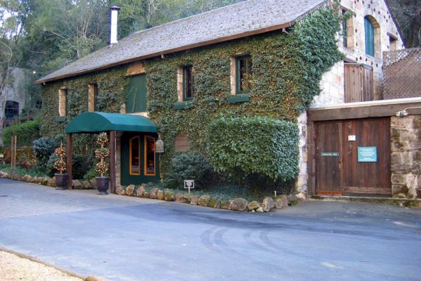 An ivy-covered building with a green awning over the entrance, a wooden door, and surrounding greenery in a rural setting, is shown.