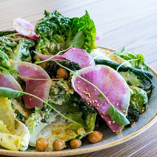 A fresh salad featuring leafy greens, chickpeas, radish slices, and a sprinkle of sesame seeds, served on a round plate.