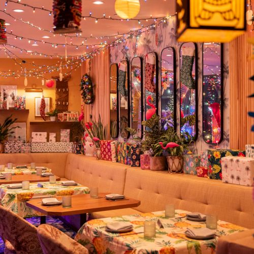 A cozy and colorful restaurant interior with decorative lights, floral patterns, and table settings ready for dining, creating a festive atmosphere.