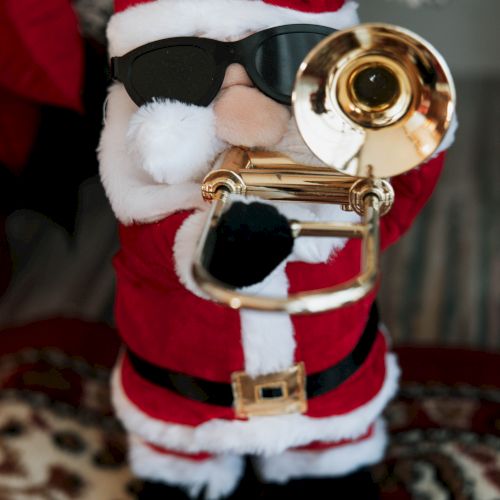 A Santa Claus figurine dressed in red and white with black sunglasses, playing a golden trombone on a patterned rug.