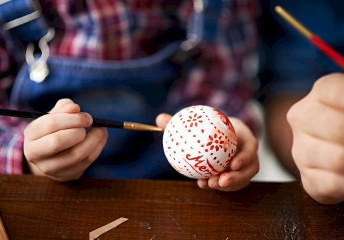 A person is hand-painting a Christmas ornament with red paint, holding it carefully with one hand while using a brush in the other hand.