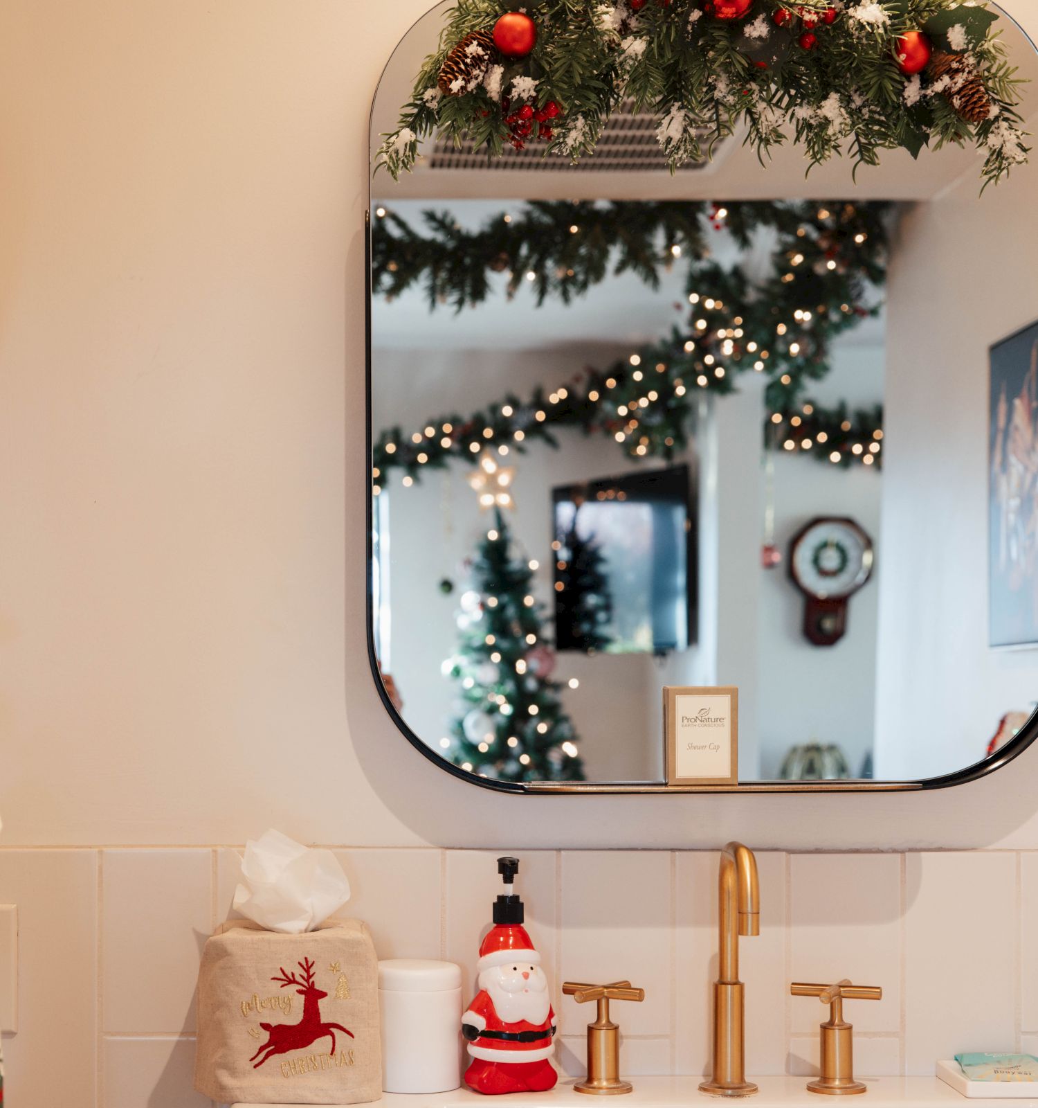 A festive bathroom features a mirror with Christmas garland, a reindeer stocking, Santa soap dispenser, and a snowman figurine on the counter.