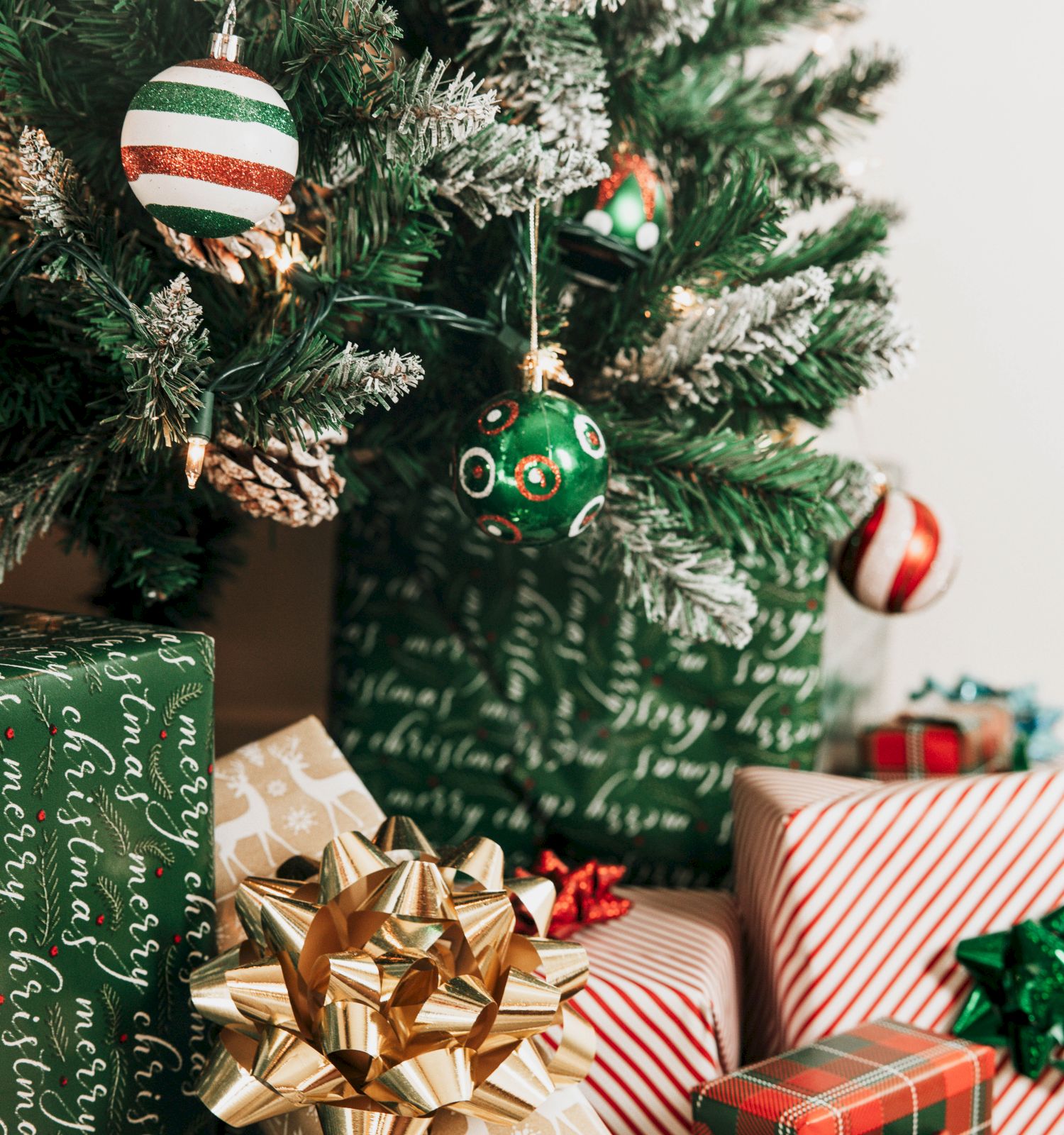 A decorated Christmas tree with ornaments and numerous wrapped gifts, featuring festive patterns and ribbons, beneath it.