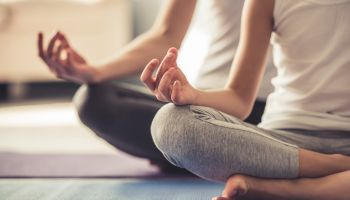 Two people are practicing yoga, sitting cross-legged on mats with their hands in a meditation gesture, focusing on mindfulness.