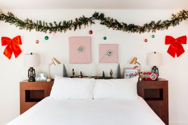 A bed with white linens in a festive bedroom, decorated with garlands, bows, ornaments, and small Christmas-themed figurines ending the sentence.