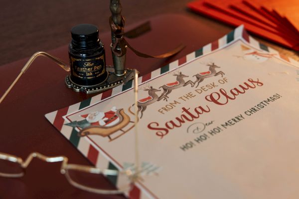 A festive letter from Santa Claus with glasses, a pen, and ink on a desk. The letter reads 