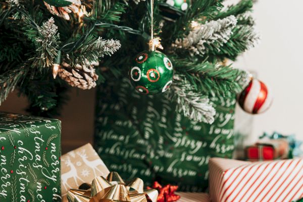 A decorated Christmas tree with various ornaments and multiple wrapped gifts with festive wrapping paper and bows placed underneath.