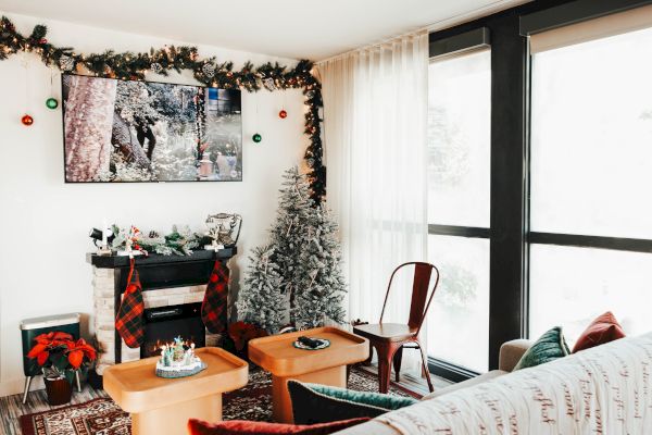 A cozy living room with Christmas decor, featuring a tree, garlands, fireplace, TV, and seating area in a bright, windowed space.