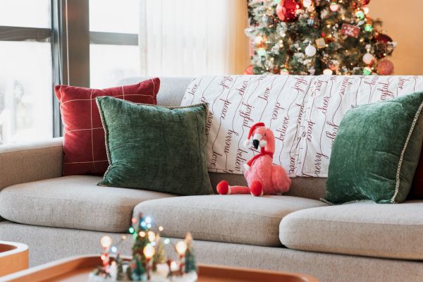 A cozy living room with festive pillows, a pink flamingo plush, and a decorated Christmas tree in the background.