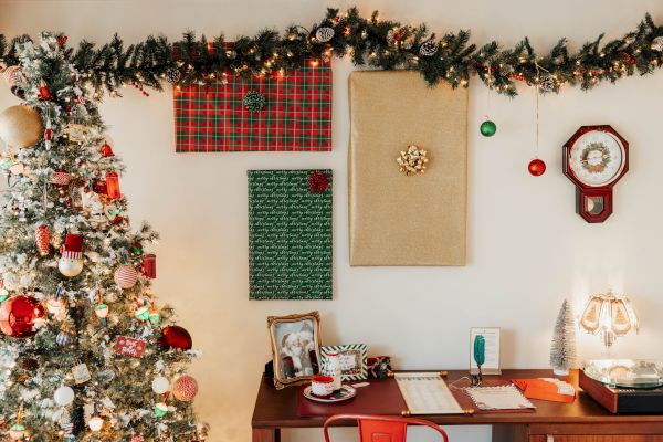 A decorated Christmas tree, festive garland, wall clock, and a desk with holiday-themed items and a lamp are displayed in the image.