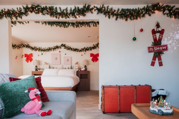 A festive room with Christmas decorations, garlands, red bows, and a holiday cake. A pink flamingo plushie sits on a green pillow.