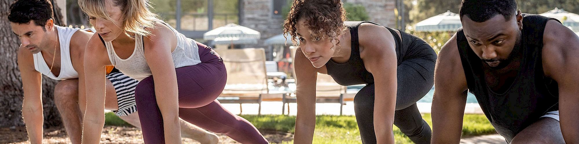 Four people are outdoors on yoga mats, appearing to be engaged in a yoga or fitness class.