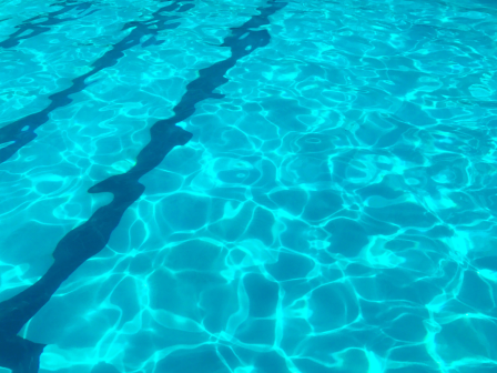 The image shows the clear blue water of a swimming pool with black lane markers visible on the bottom of the pool.