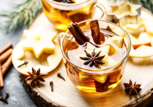 A warm beverage in a glass cup with cinnamon, star anise, and apple slices on a wooden surface.