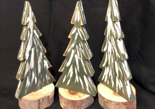 The image shows three small decorative Christmas trees with snow, each standing on a wooden base against a dark background, possibly for festive decor.