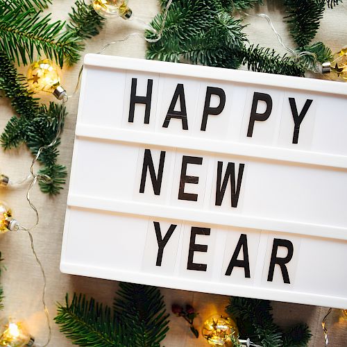 A lightbox sign says "HAPPY NEW YEAR" surrounded by green pine branches and festive string lights, creating a celebratory atmosphere.