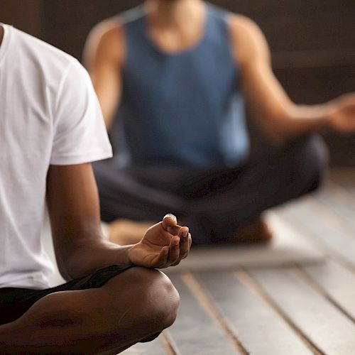 Several people are seated on yoga mats, meditating with one individual in a white shirt and the others out of focus.