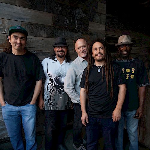 A group of five diverse men standing in front of a wooden wall, casually dressed, some smiling.