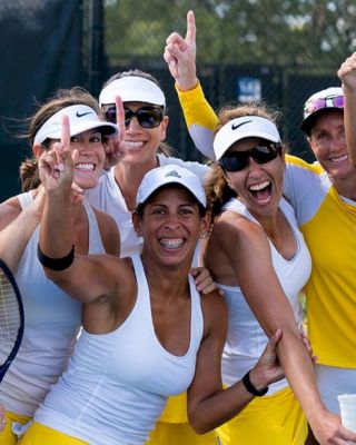 A group of women in yellow and white sportswear, holding tennis rackets and smiling, stands on a tennis court posing for a photo.