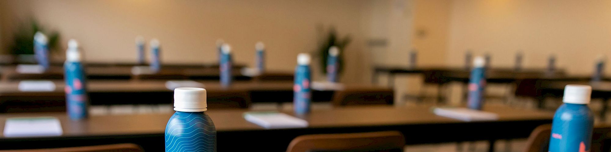 A conference room setup with tables and chairs featuring bottled water and notepads at each seat, ready for attendees.