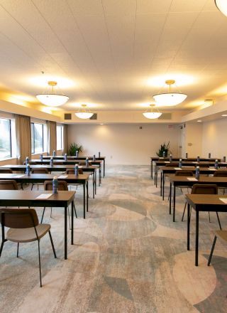 A conference room set up classroom-style with long tables, chairs, water bottles, large windows, and well-lit overhead lights ending the sentence.