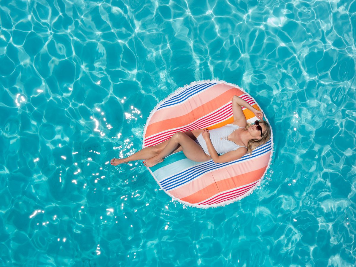 A person is relaxing on a colorful striped float in a clear blue pool, enjoying the sunny weather.