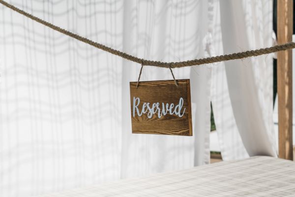 A wooden "Reserved" sign hangs on a rope in front of a white curtain, indicating a reserved area or space.