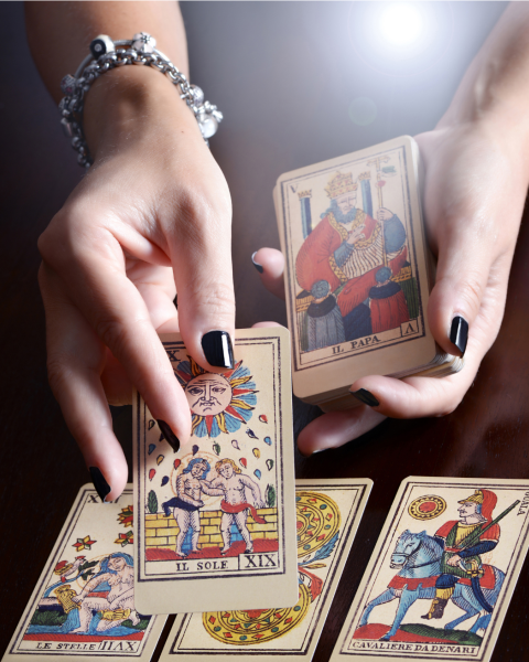 A person's hands are holding and displaying tarot cards on a table, with several tarot cards spread out in front.