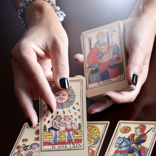 A person's hands are holding and displaying tarot cards on a table, with several tarot cards spread out in front.