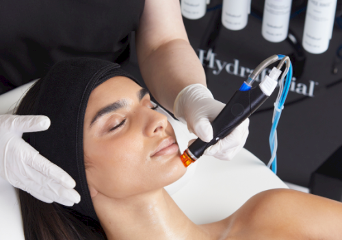 A person is receiving a professional facial treatment with a specialized device while lying on a table, performed by someone in a clinic.