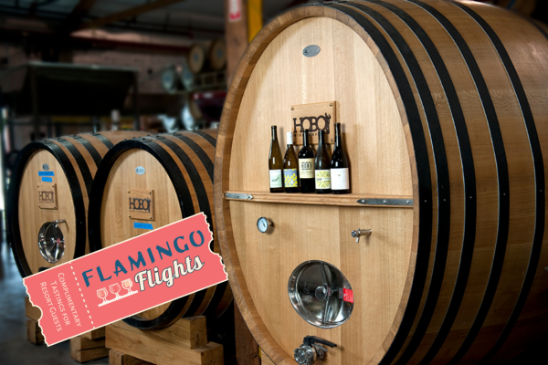 The image shows large wooden wine barrels, some with wine bottles on them, and a "Flamingo Flights" ticket in the foreground.