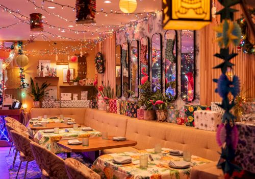 A vibrant, decorated restaurant interior with colorful lights, plants, and floral patterns, featuring tables set for dining.