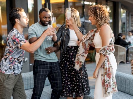 Four people are standing outside, smiling, and raising their glasses in a toast. They appear to be enjoying a social gathering.