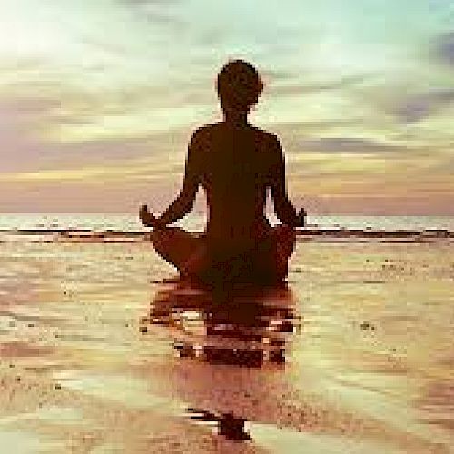 A person meditates in a cross-legged position on a tranquil beach at sunset, reflecting a serene landscape and calm atmosphere.