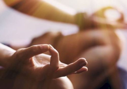 The image shows a close-up of hands in a meditation pose, with fingers forming a mudra, and sunlight streaming in.