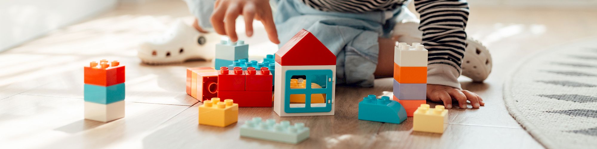 A child is playing on the floor with colorful toy building blocks in a sunlit room.