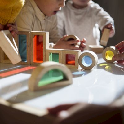 Children are playing with colorful translucent blocks on a light table, exploring shapes and colors together.